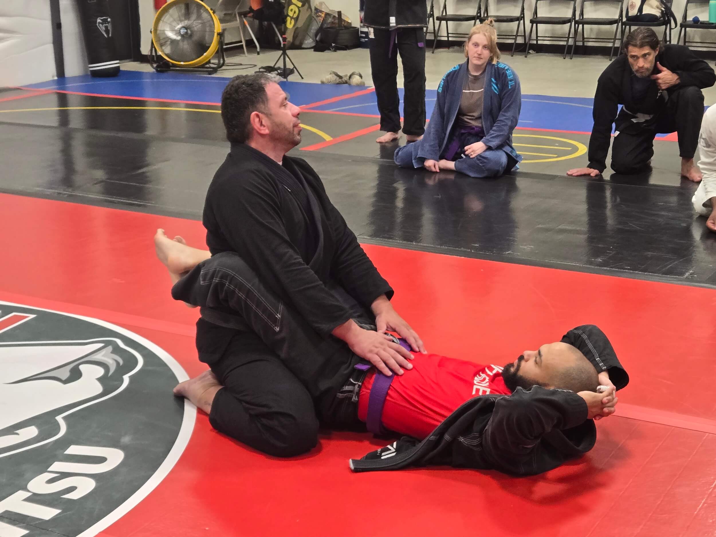 Ruffhouse Jiu-Jitsu instructor demonstrating proper BJJ techniques with student during adult class.